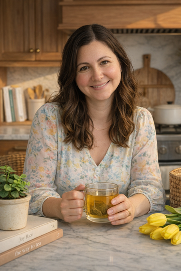 Aligned Herbals founder holding a glass mug of organic herbal tea in a warm kitchen